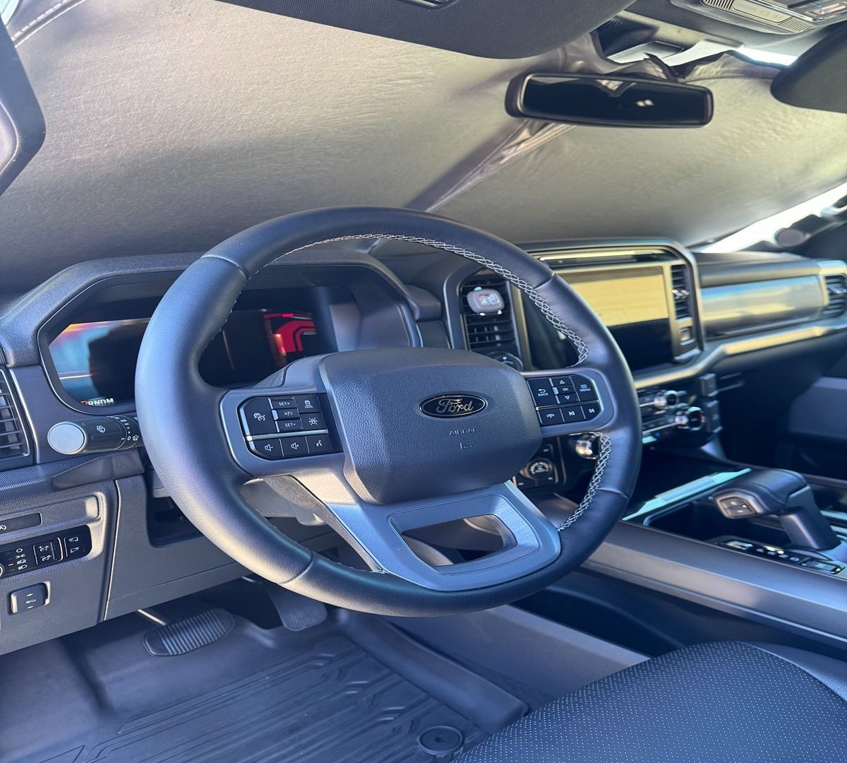 Interior view of a modern Ford truck cabin featuring a leather steering wheel, digital dashboard, and a sunshade.