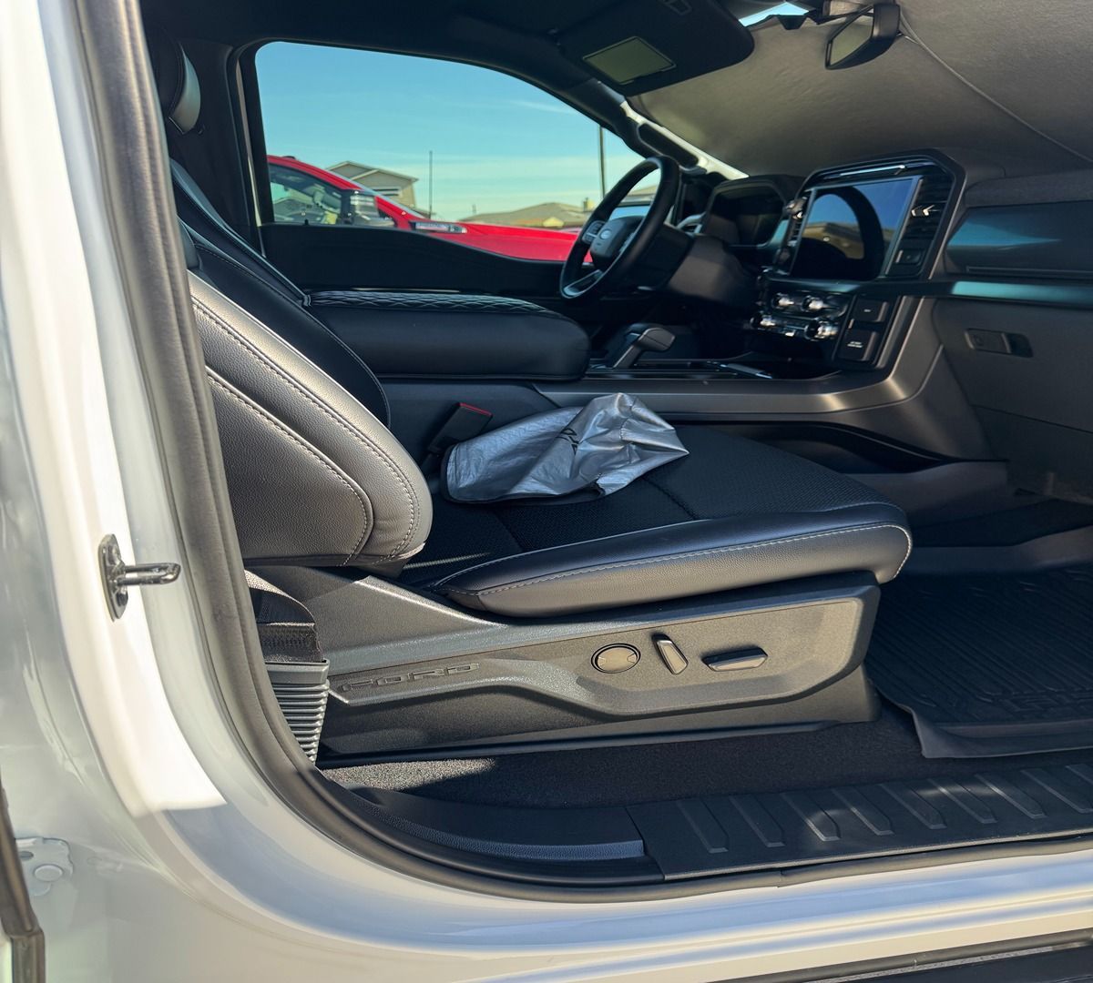 Interior view of a vehicle's front passenger seat and dashboard with black leather upholstery and digital displays.