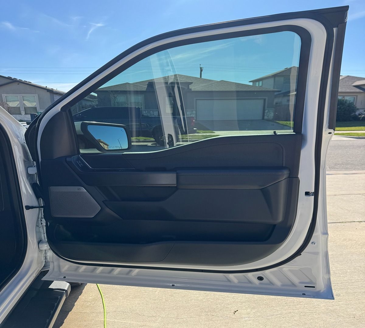 The open driver-side door of a white vehicle, showing a dark gray interior panel and a window with a blue-tinted film.