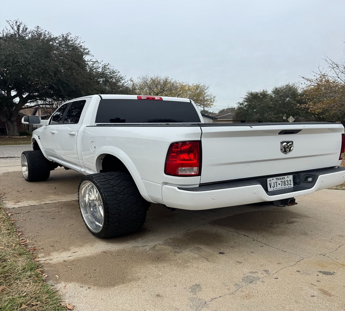 A white RAM pickup truck parked on a concrete driveway with large, wide-rimmed wheels extending past the body.