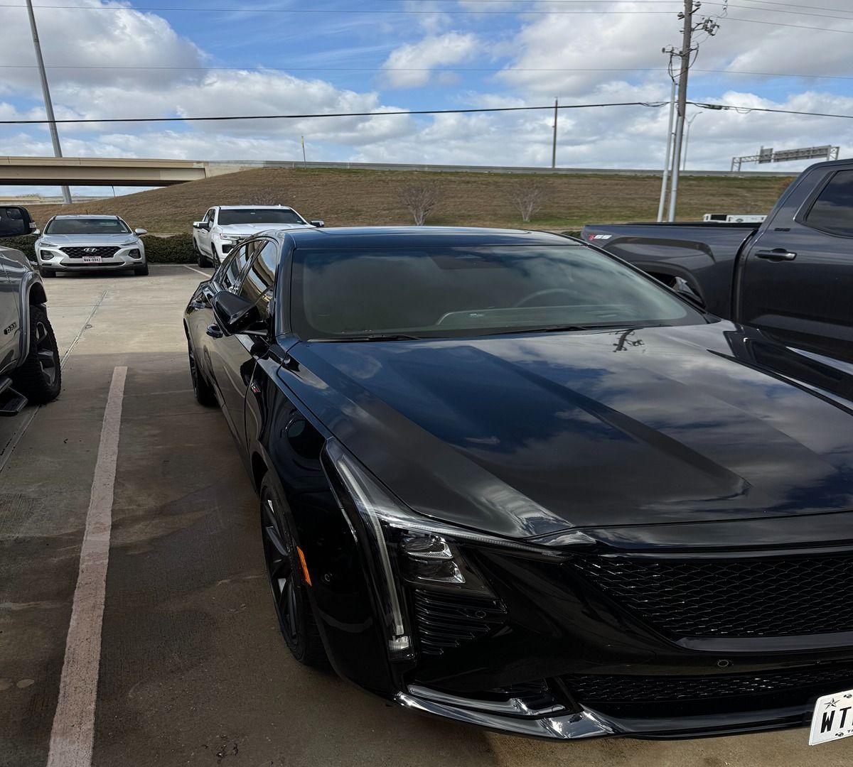 A black Cadillac CT5-V parked in a lot during the day, viewed from the front passenger side.