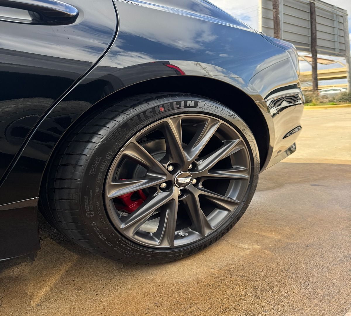 Close-up of a black luxury car's rear wheel with multi-spoke dark grey rims, Michelin tires, and red brake calipers.