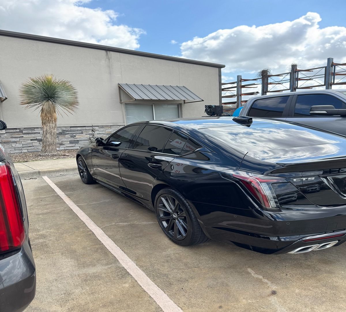 A black Cadillac sedan parked in a parking lot next to a light-colored building under a partly cloudy sky.