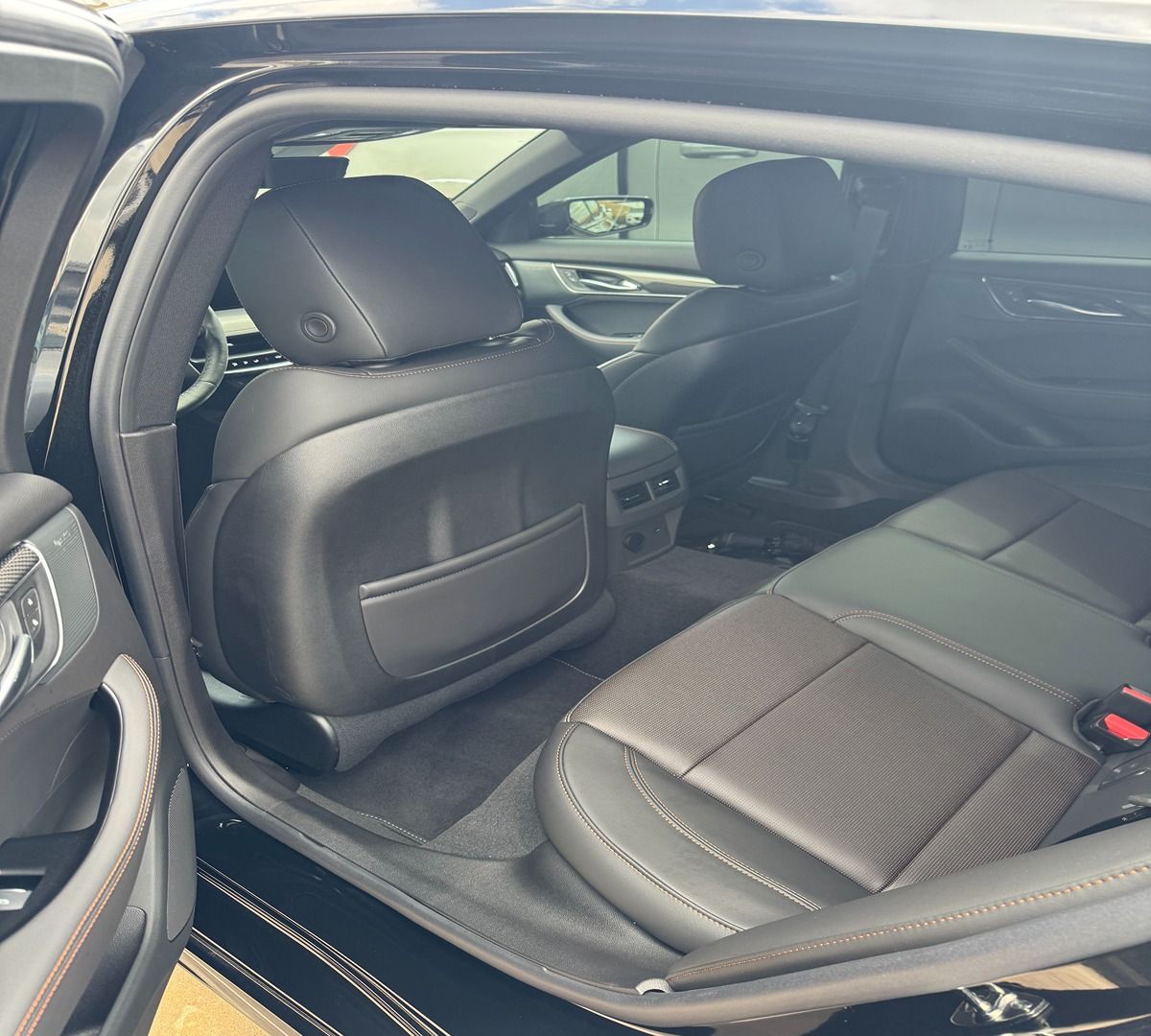 The interior of a car's back seat, featuring black leather upholstery and a pocket on the back of the front seat.