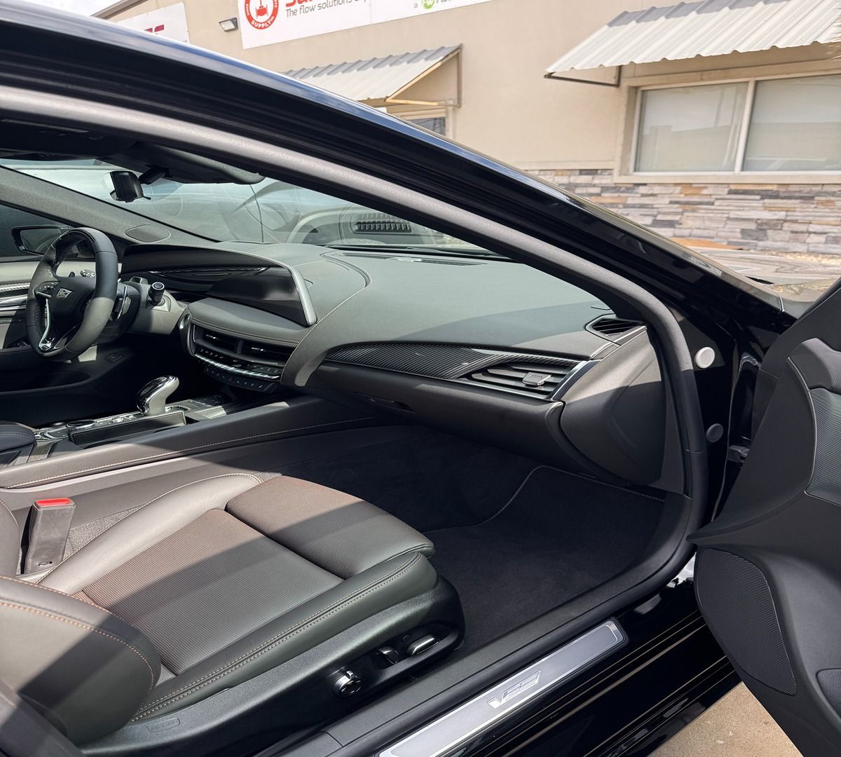 The interior of a black vehicle showing the front driver's seat, steering wheel, and dashboard from an open door view.