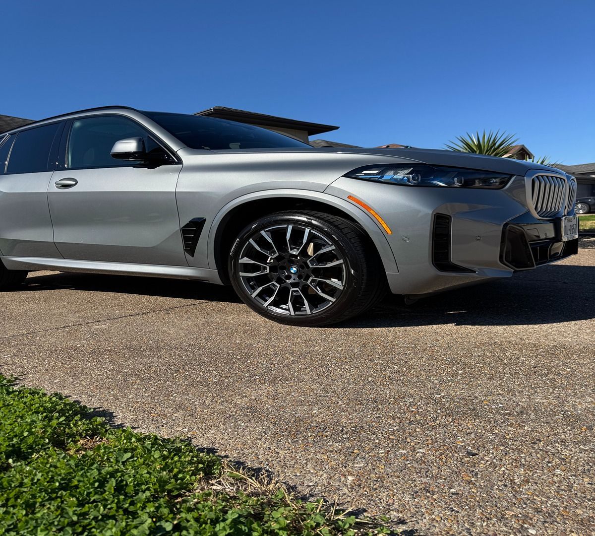 A silver BMW SUV parked on a textured gravel driveway under a clear blue sky.