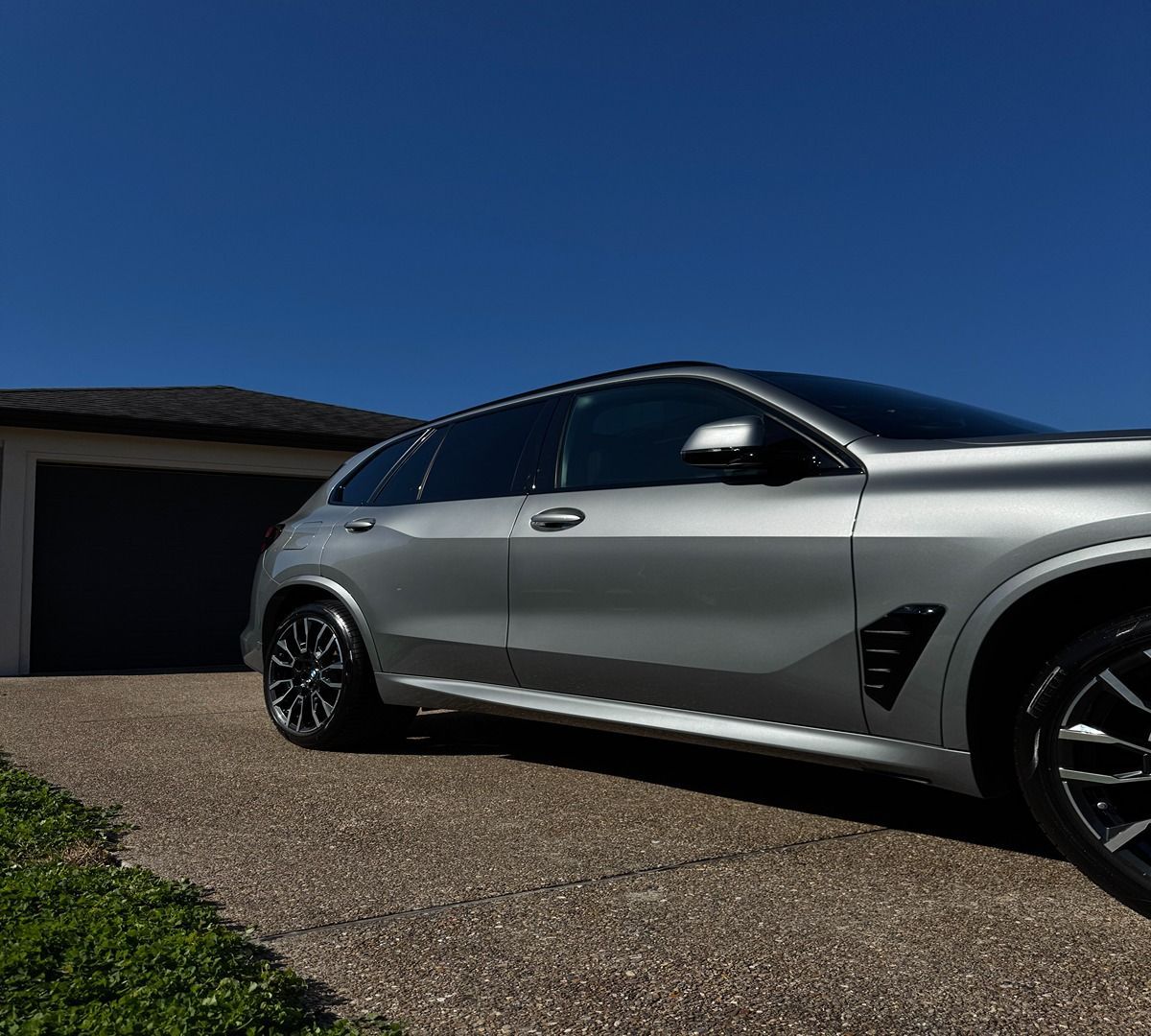 A silver BMW SUV parked on a residential driveway on a clear, sunny day.
