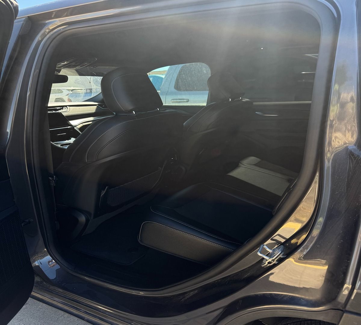 Interior view of a dark-colored vehicle showing the back seats and legroom through an open door.