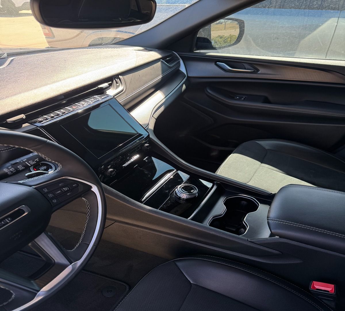 The interior of a modern black car, showing the driver's seat, steering wheel, central touchscreen, and dashboard.