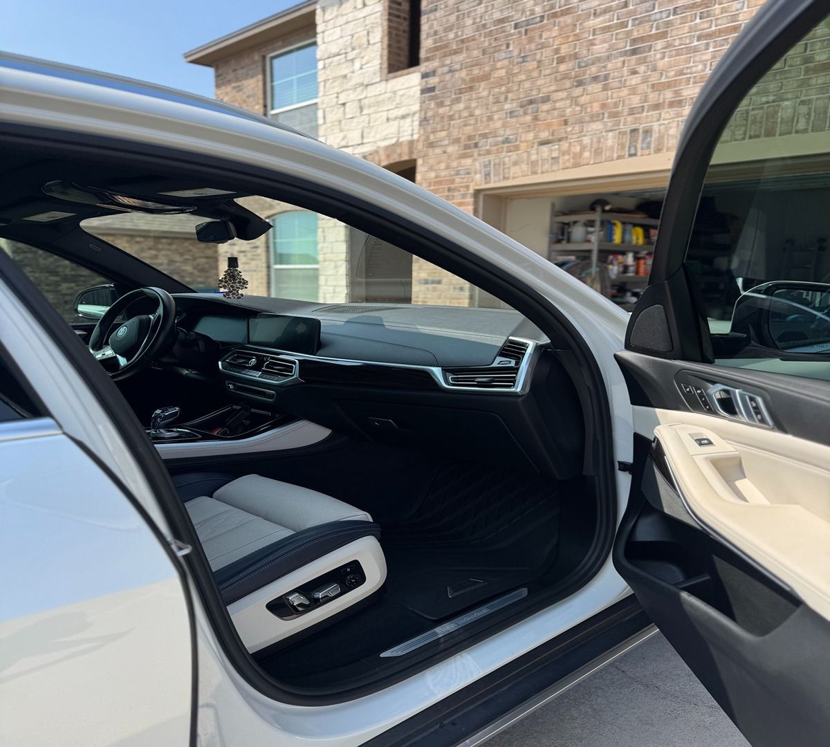 Interior of a modern BMW featuring a black and white leather seat and dashboard, viewed through an open car door.
