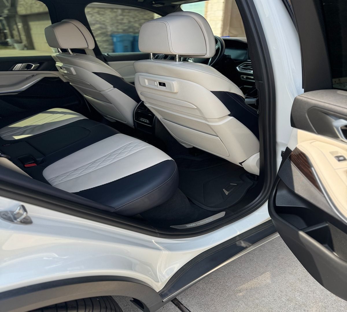 The rear interior of a white SUV with two-tone cream and dark blue leather seats and open doors.