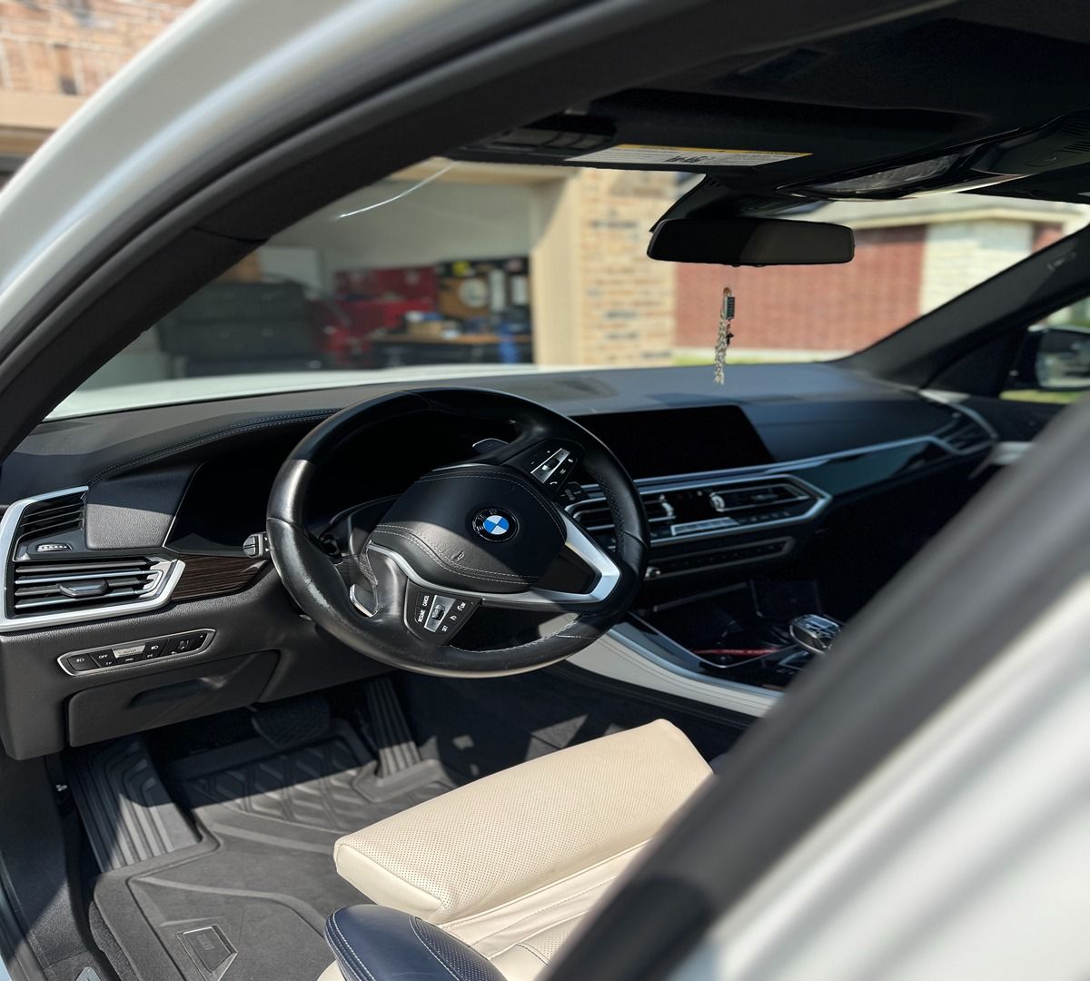 The interior cabin of a BMW SUV, featuring a black dashboard, steering wheel, and cream-colored leather seats.
