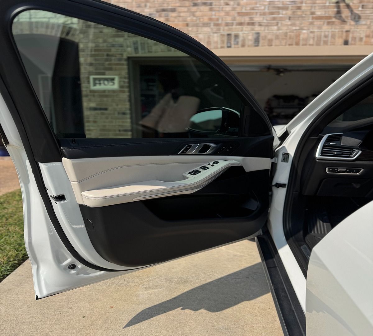 The open front door of a white luxury car, revealing a cream and black leather interior, parked on a residential driveway.