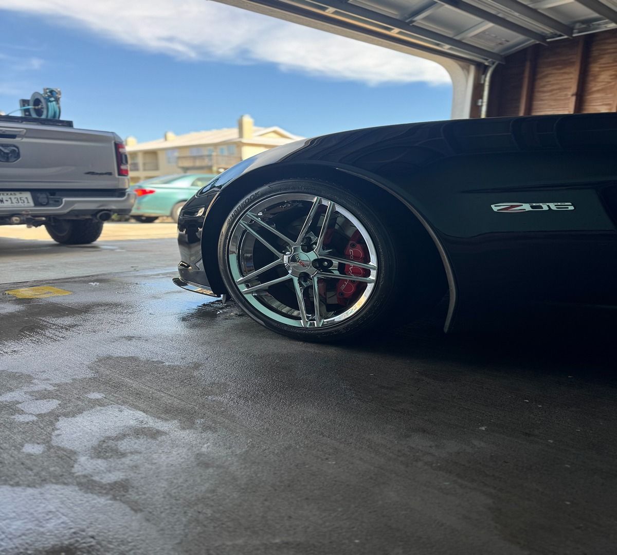 A black Corvette ZR1 parked in a garage, featuring chrome wheels with red brake calipers, with a truck visible outside.