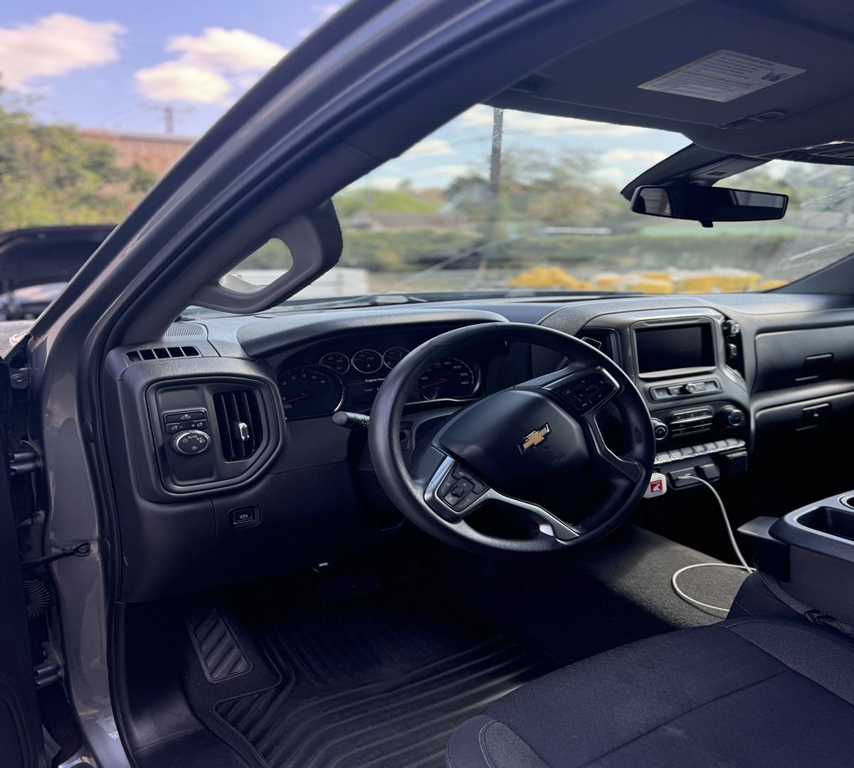 The interior of a grey Chevrolet pickup truck showing the steering wheel, dashboard, and driver-side floor mat.