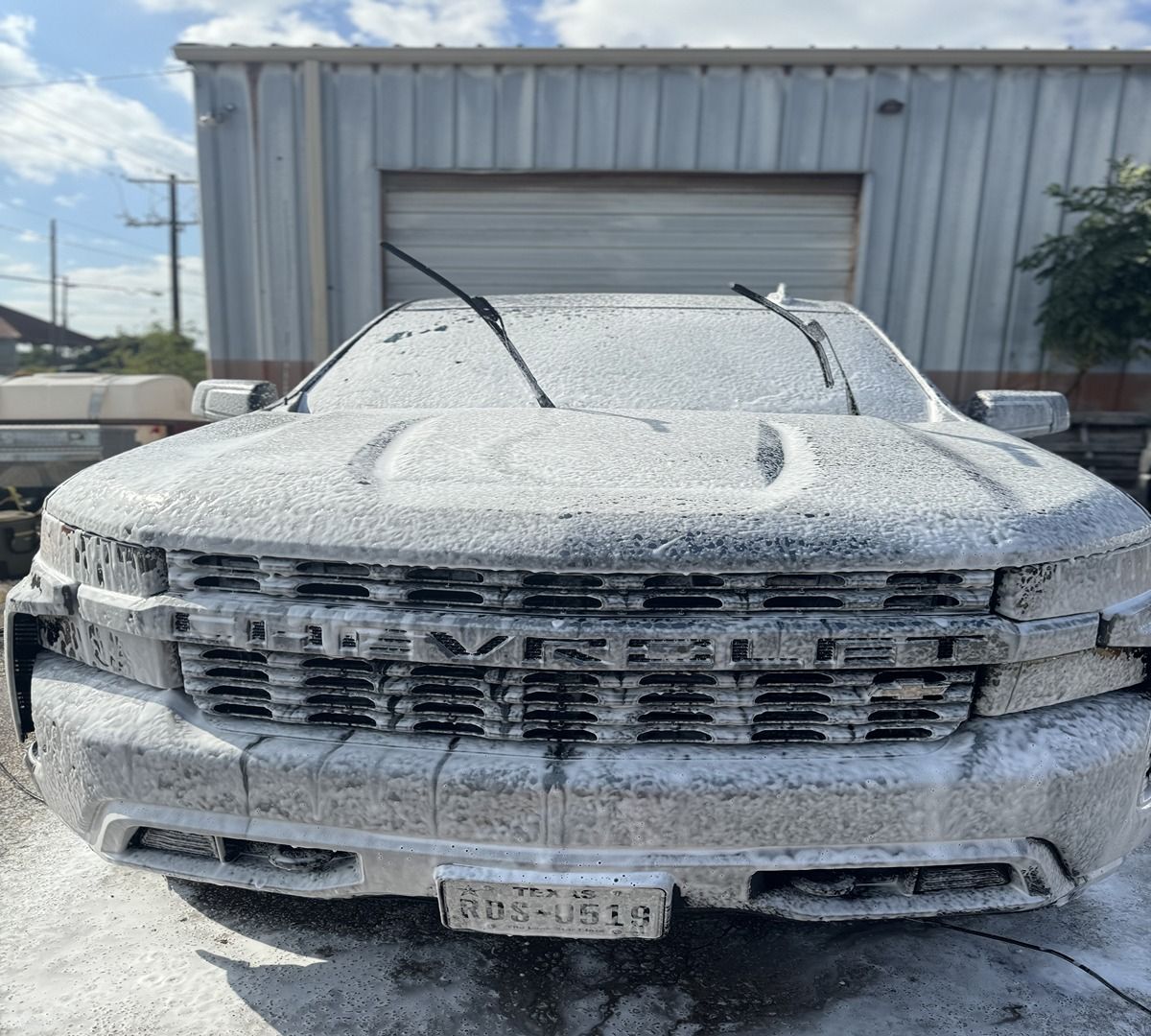 A white Chevrolet pickup truck covered in thick, white soap suds at a car wash.