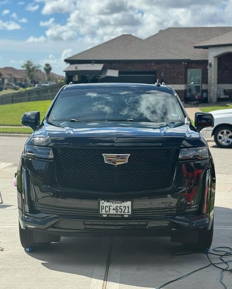 Front view of a shiny black Cadillac SUV parked in a residential driveway on a sunny day.