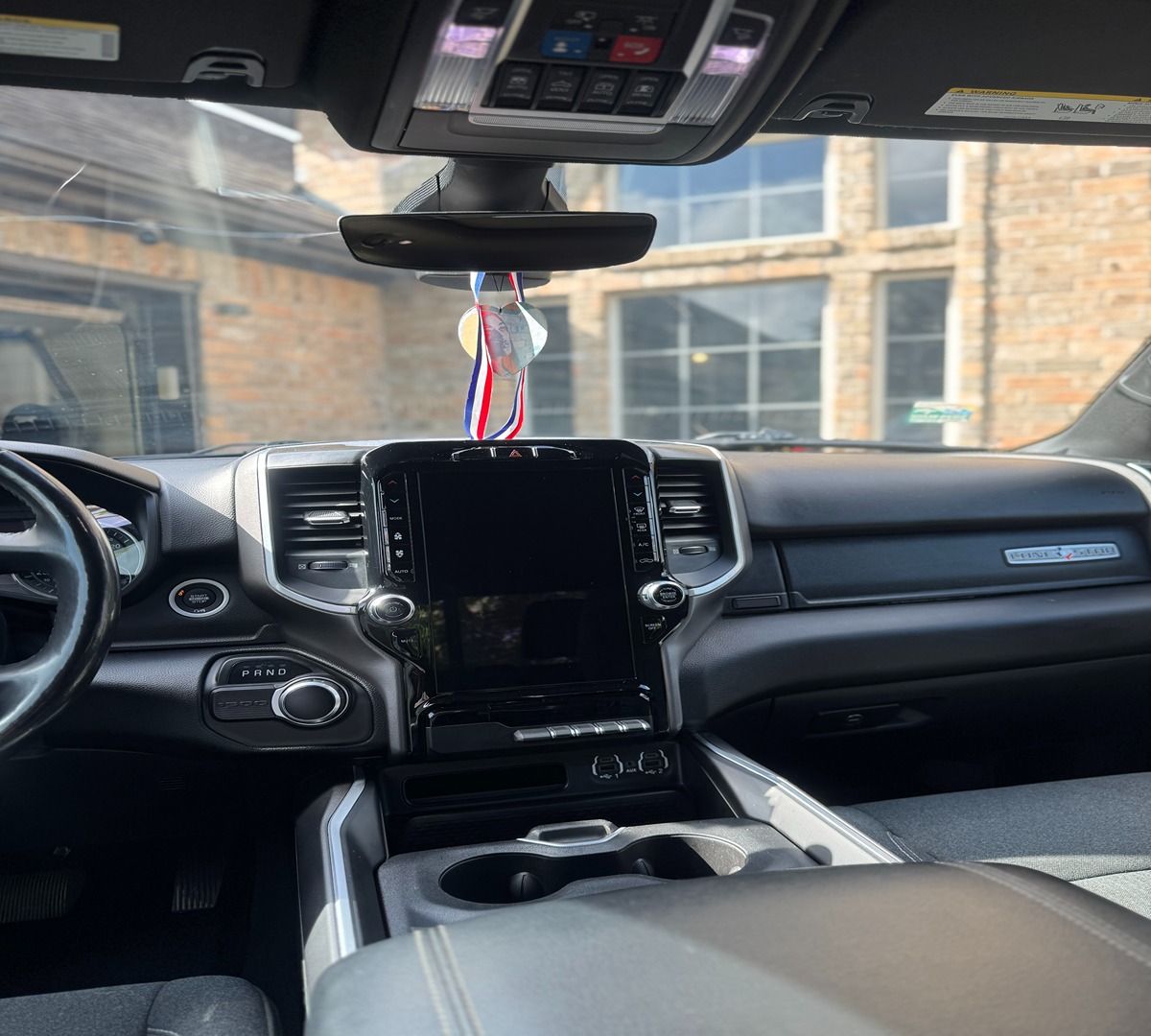 Dashboard of a truck interior, featuring a central touchscreen display, steering wheel, and a hanging ornament.