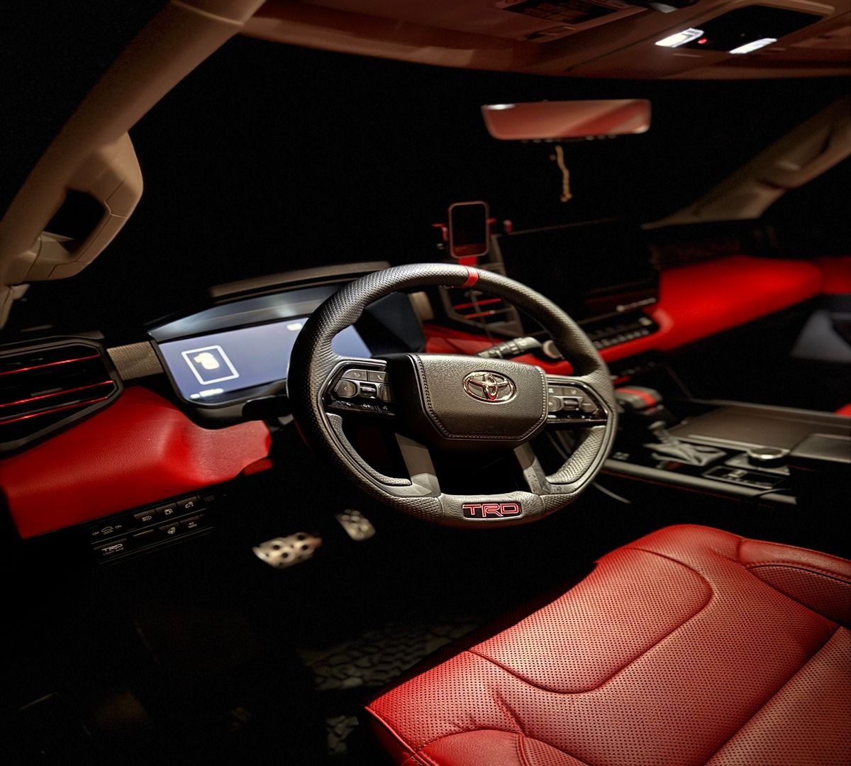 Modern car interior featuring a black and red leather cabin, carbon fiber steering wheel, and digital dashboard displays.