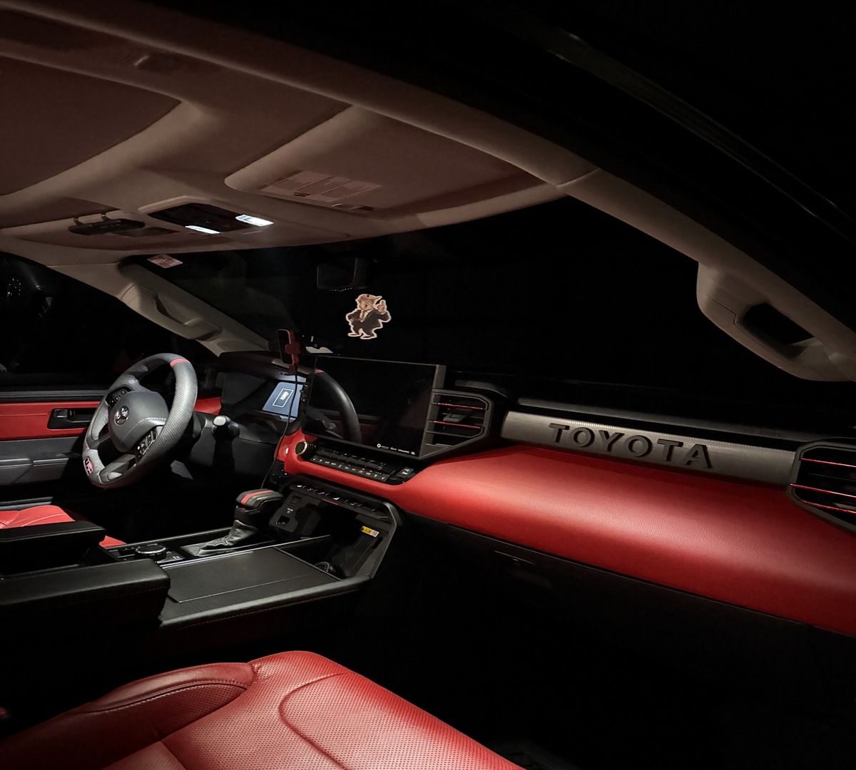 Interior of a modern Toyota truck featuring a black and red dashboard with bold silver Toyota lettering and red seats.