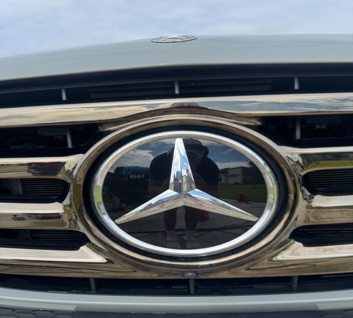 A metallic Mercedes-Benz emblem centered on a shiny, horizontal-slat car grille.