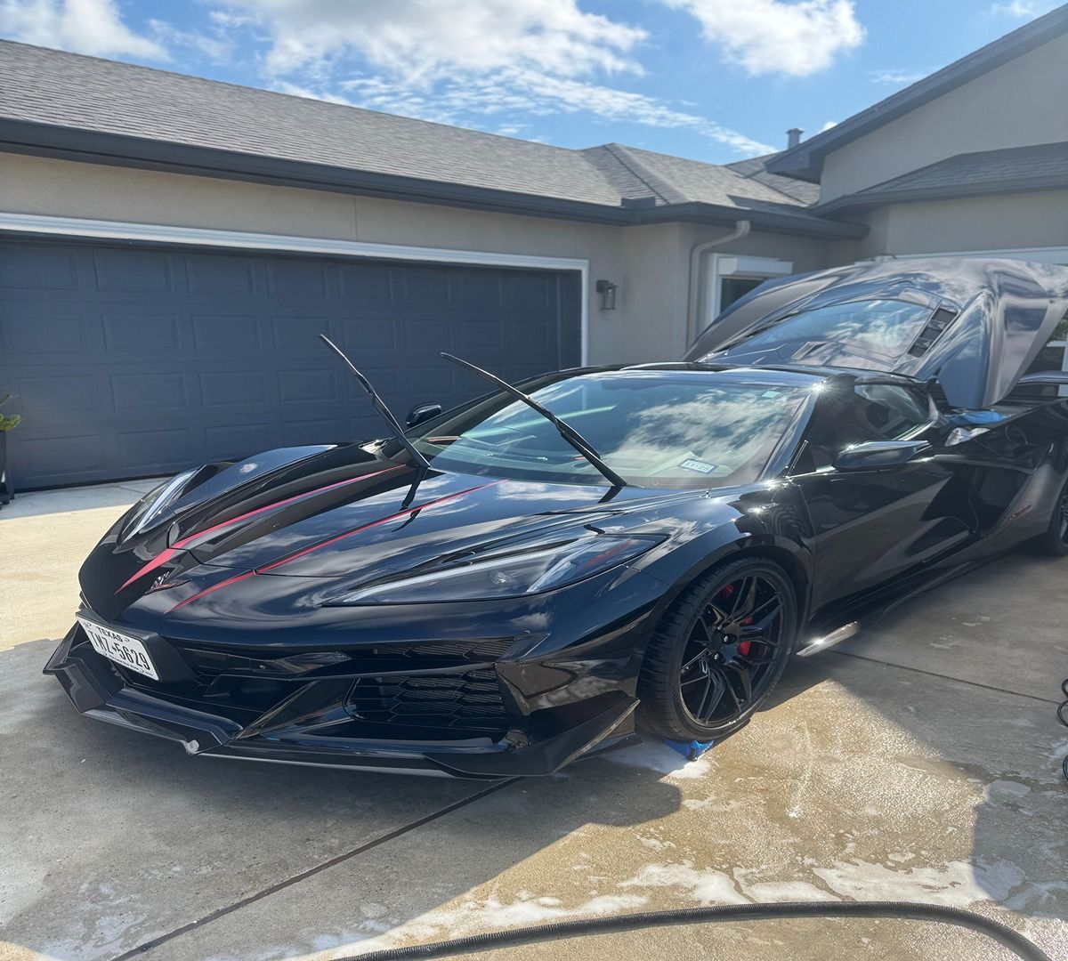 A black Chevrolet Corvette parked on a residential driveway with its windshield wipers raised.