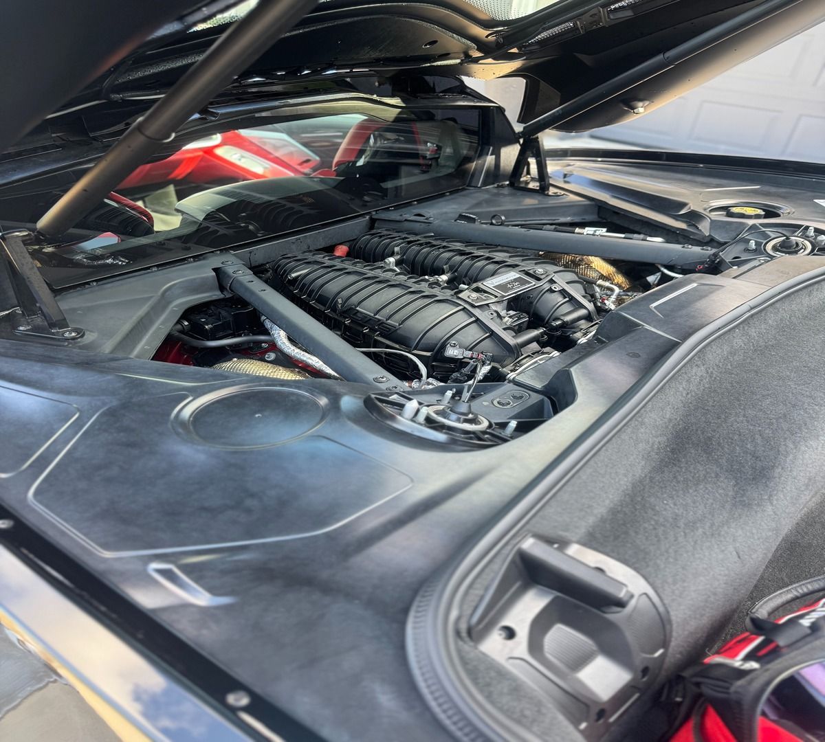 The engine compartment of a mid-engine sports car with the rear deck lid open, showcasing internal components and framing.