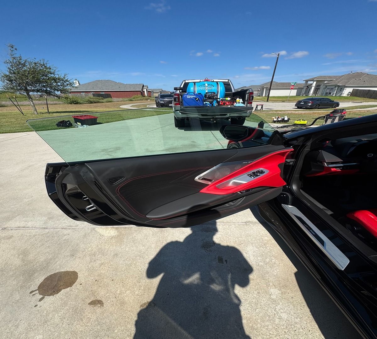A low-angle shot of an open car door with a black and red interior, parked on a residential driveway on a sunny day.