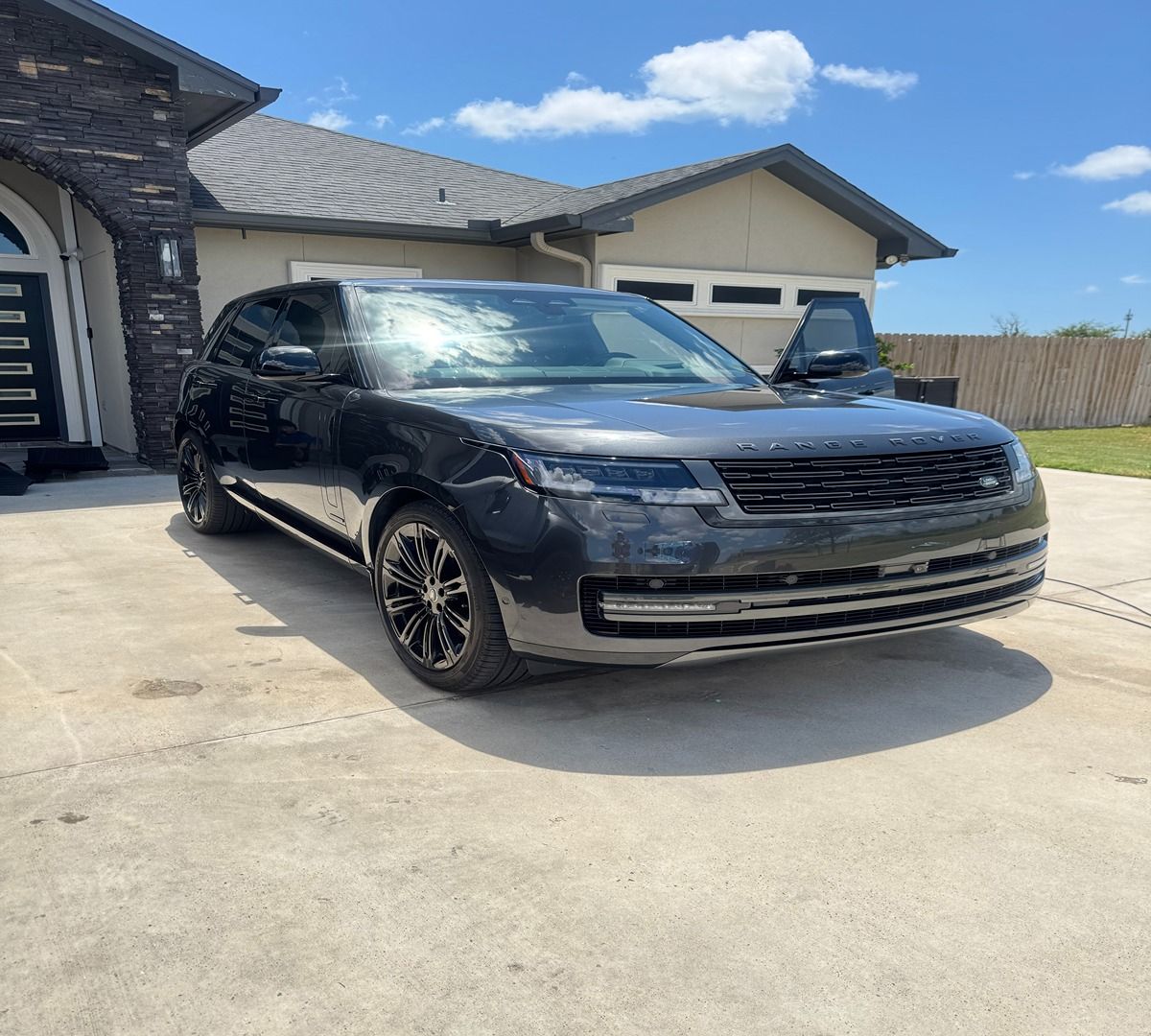 A black Land Rover Range Rover parked on a concrete driveway in front of a house on a sunny day.