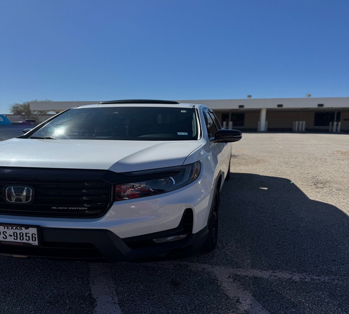 A white Honda Ridgeline truck parked in an empty outdoor gravel lot under a clear blue sky.