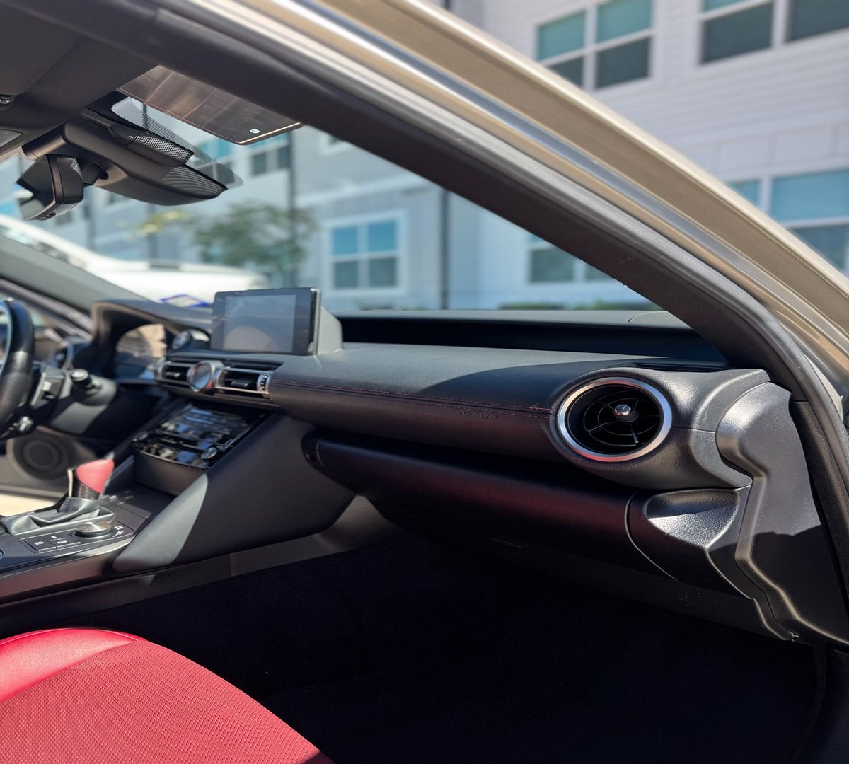 Interior view of a car cockpit featuring a black dashboard, circular air vent, and vibrant red passenger seat.