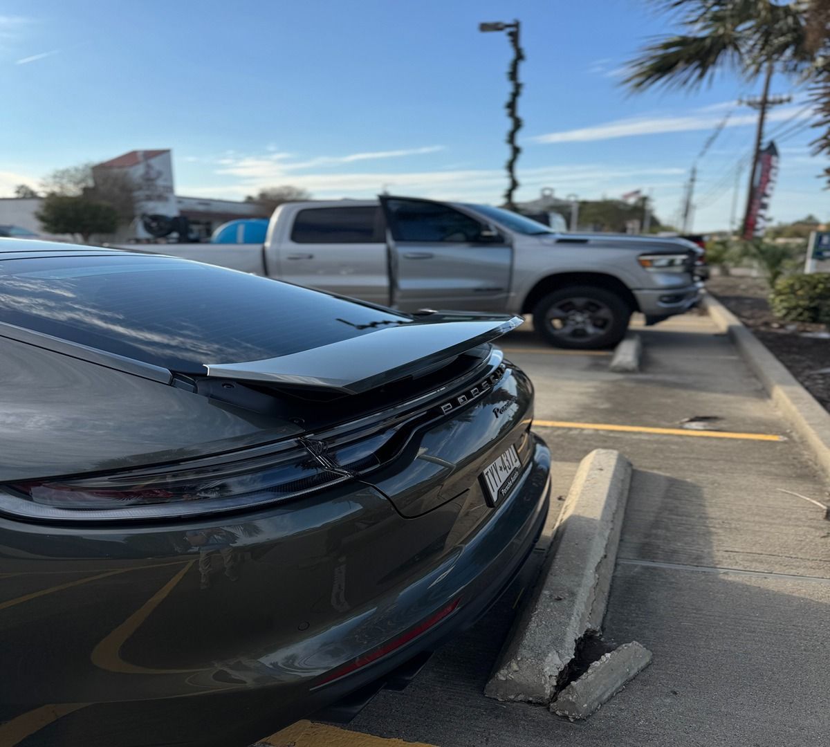 Rear view of a dark grey Porsche parked in a parking lot, with a silver truck parked behind it.