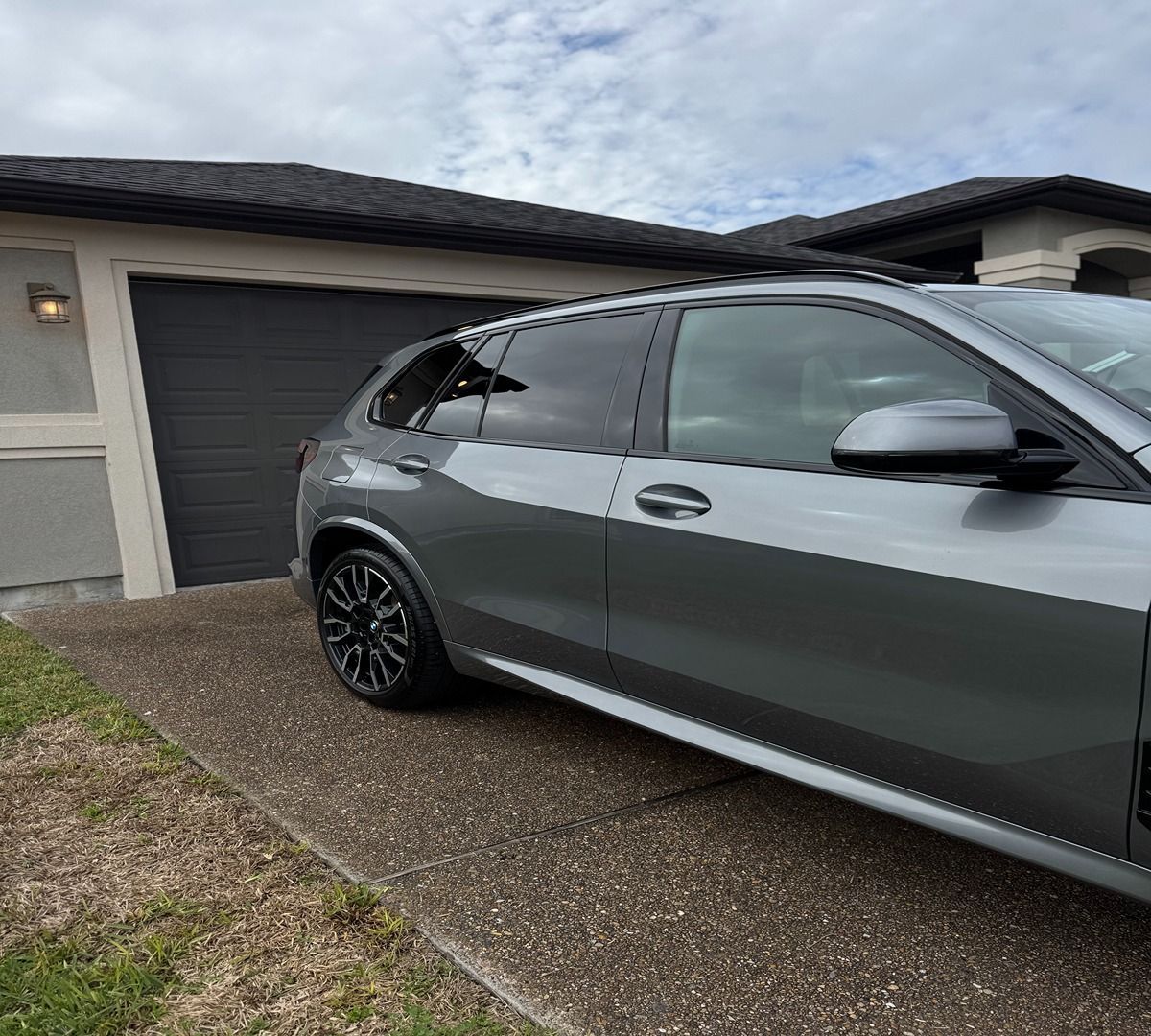 A gray SUV parked on a concrete driveway in front of a house with a dark garage door.