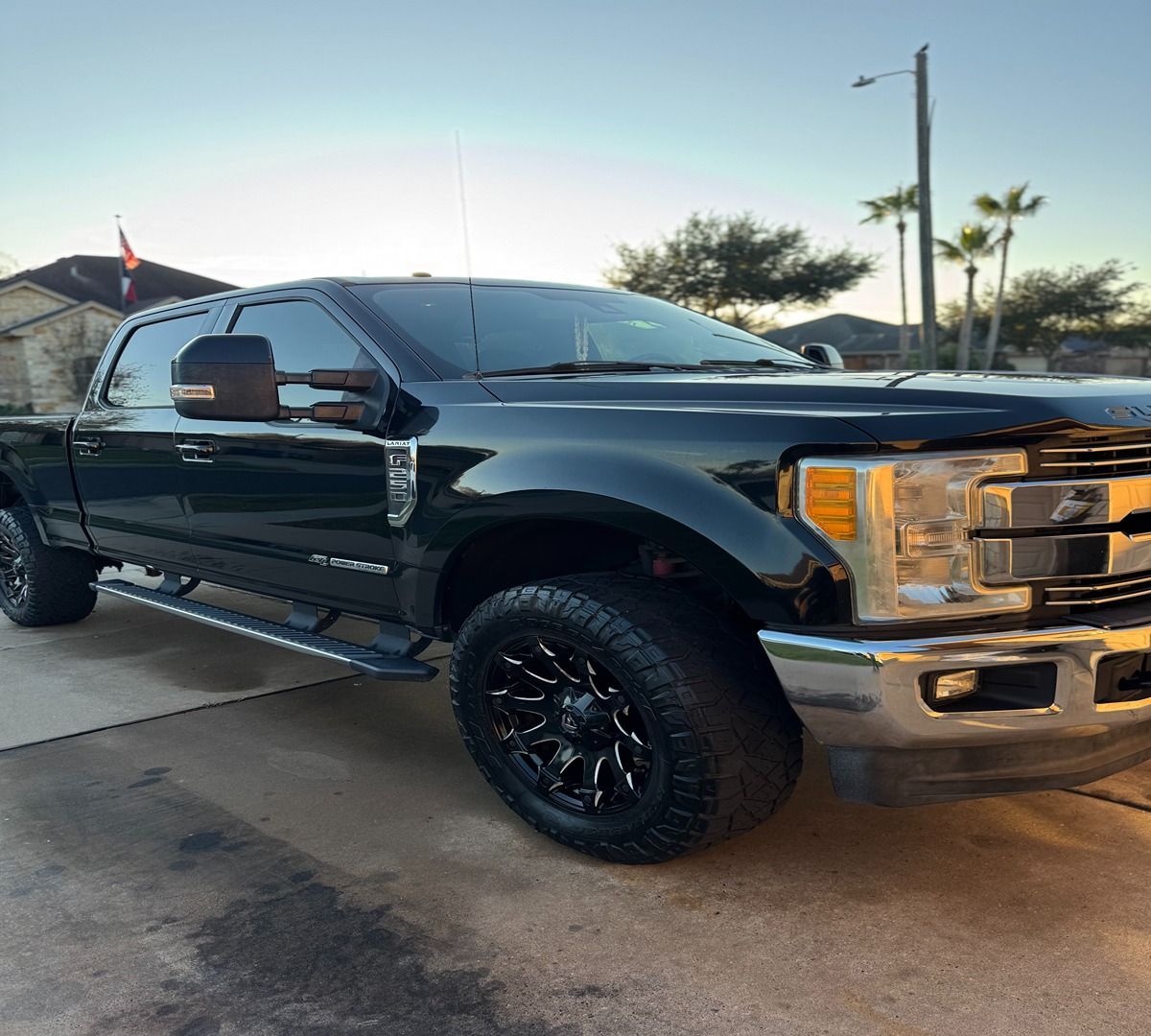 A black Ford Super Duty pickup truck parked on a concrete driveway during the day.
