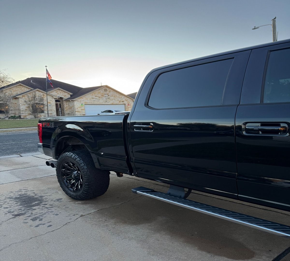 A shiny black Ford F-series pickup truck parked on a concrete driveway in a suburban neighborhood at sunset.