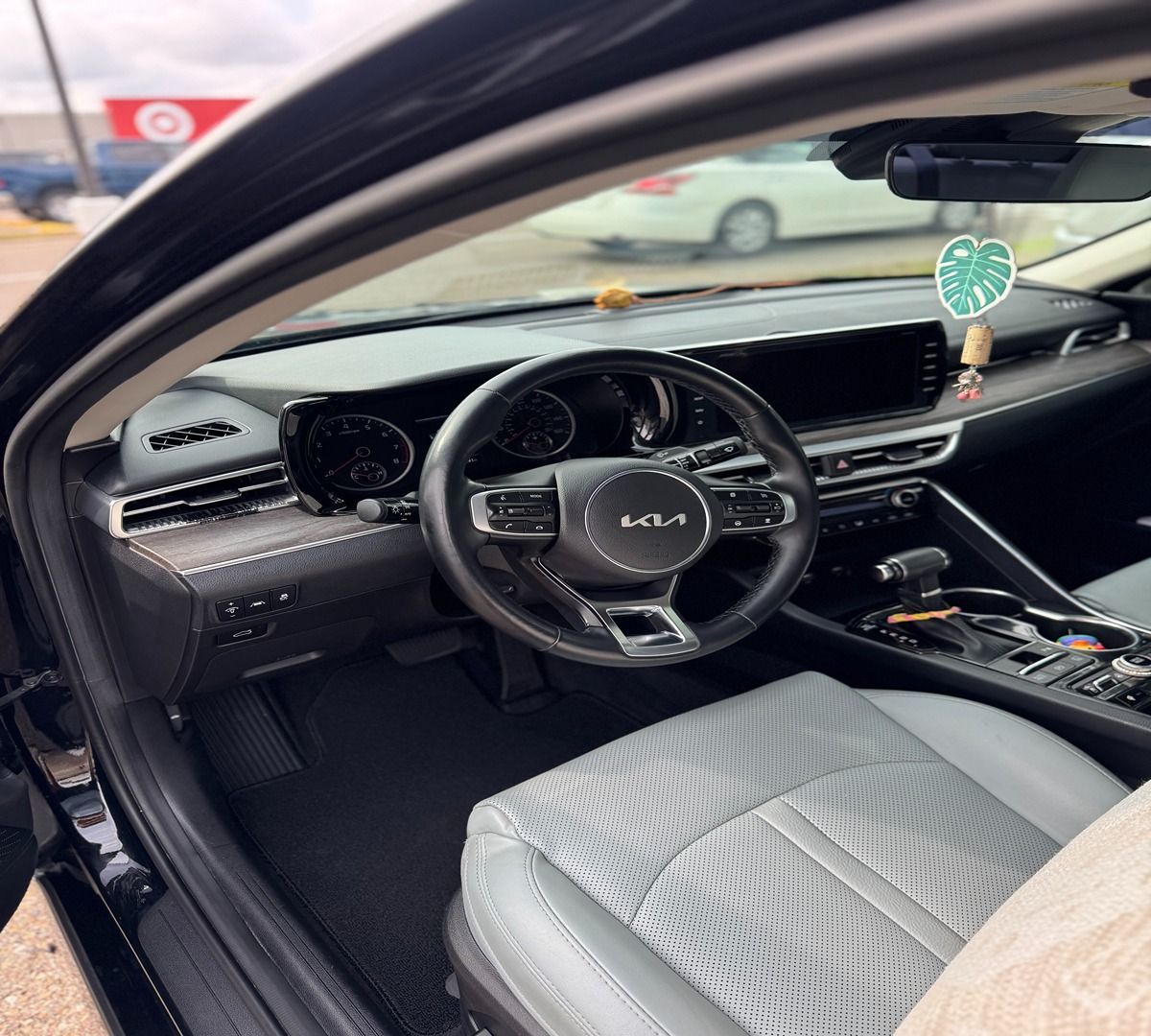 Interior view of a modern car with a black steering wheel, gray leather seats, and a digital dashboard.