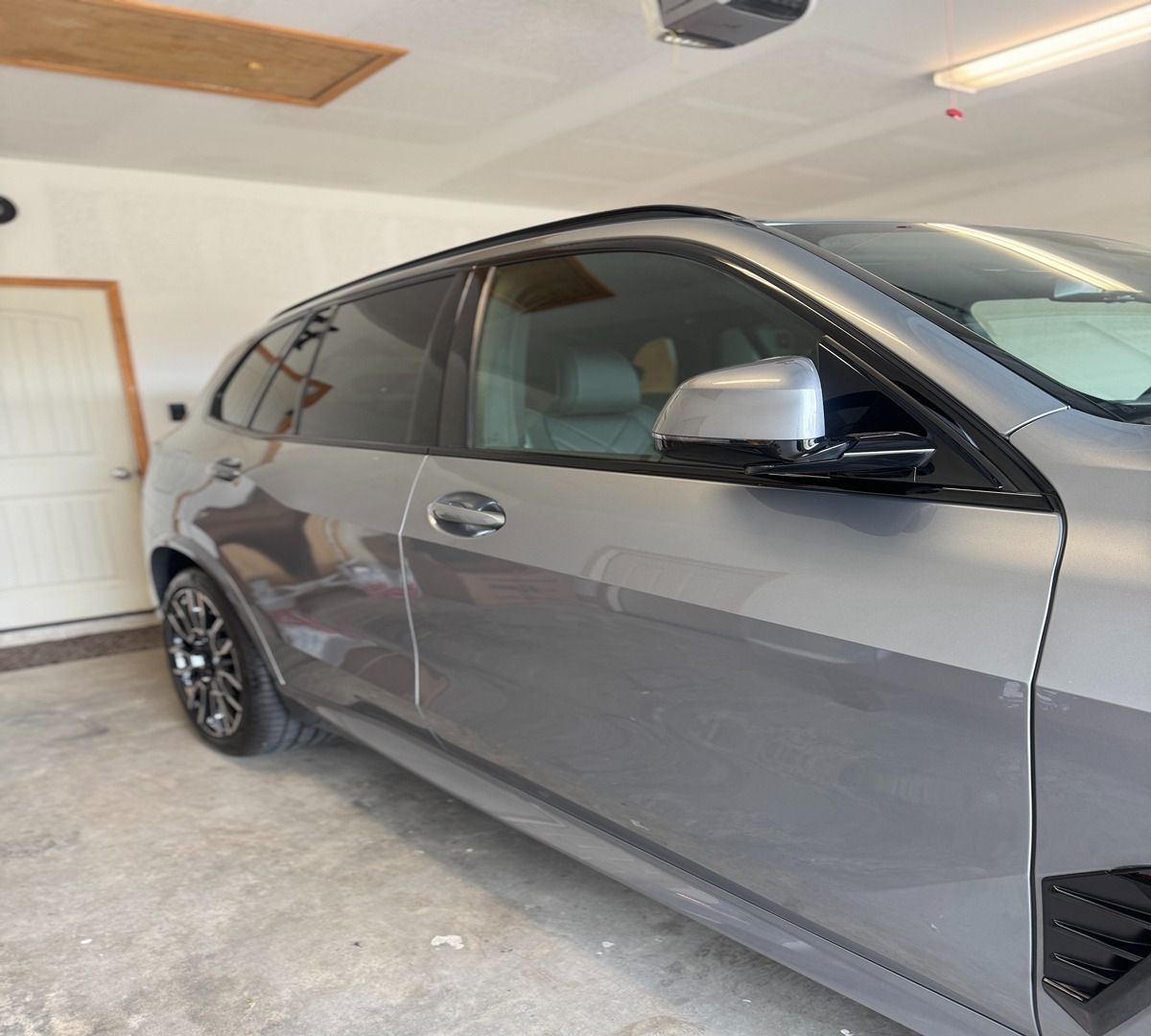 A gray luxury SUV parked in a garage, focusing on the side profile, tinted windows, and silver side mirror.