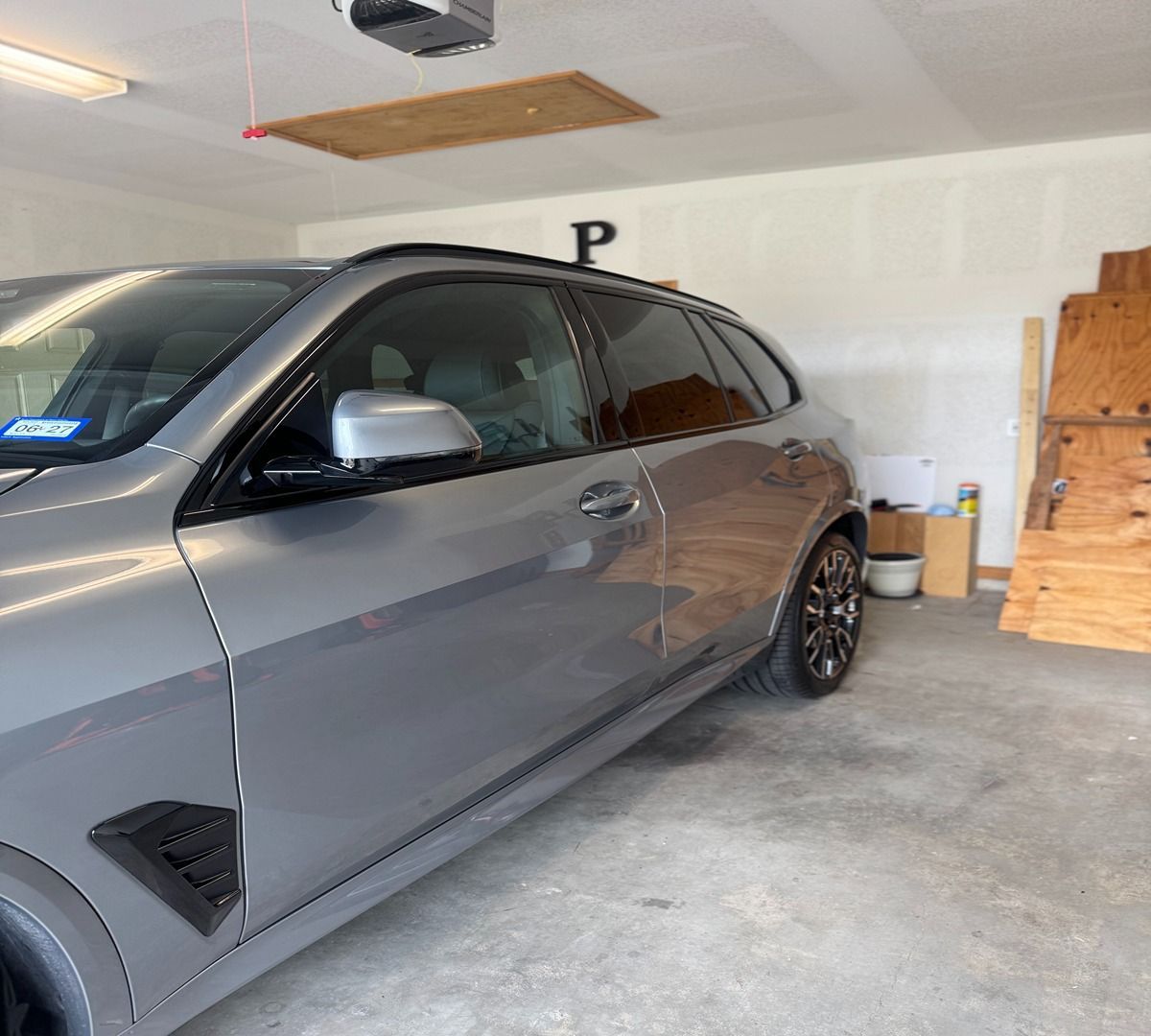 A grey SUV parked inside a garage next to stacked pieces of plywood.