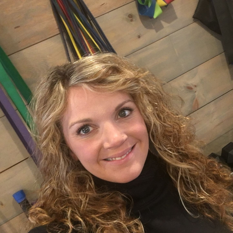 Stephanie smiles, posing in front of exercise bands and a wood background.