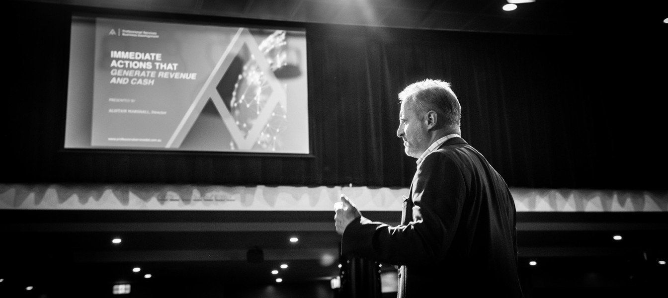 A man in a suit is giving a speech in front of a large screen.
