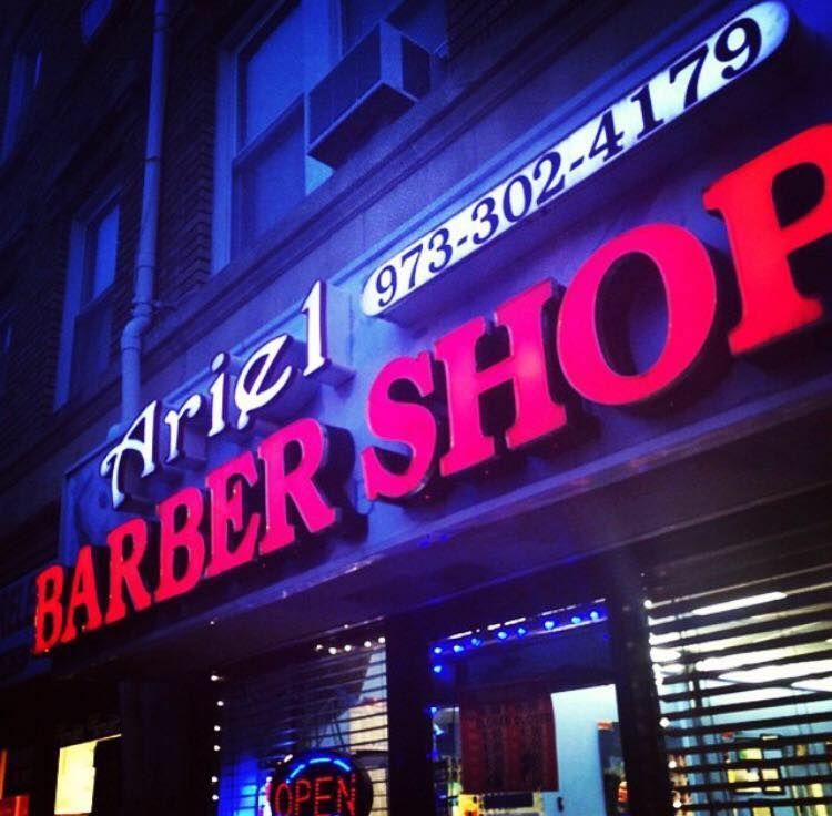 Bright neon sign for Ariel Barber Shop at night with phone number 973-302-4179