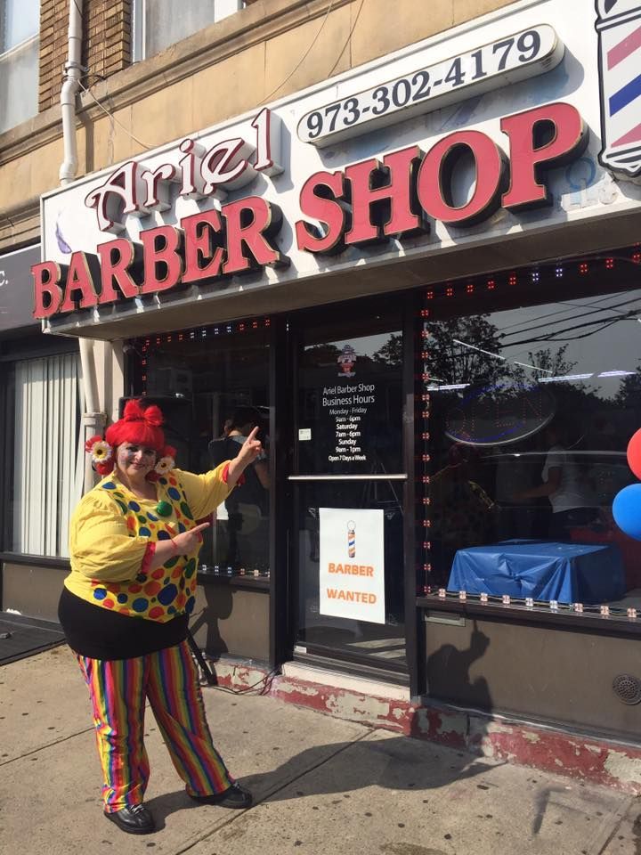 Person in colorful outfit posing outside Atria Barber Shop storefront