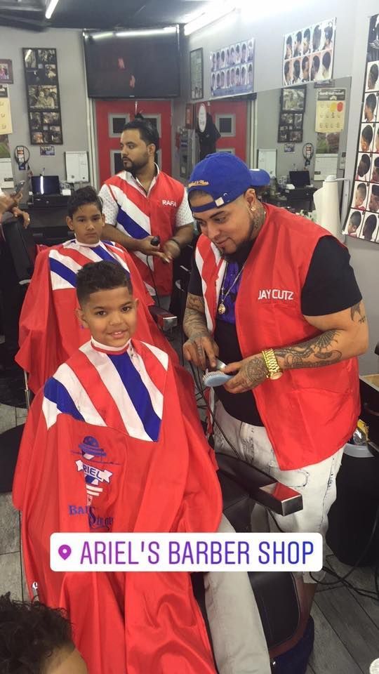 Barber shop scene with two customers in red capes and a barber working on a haircut.