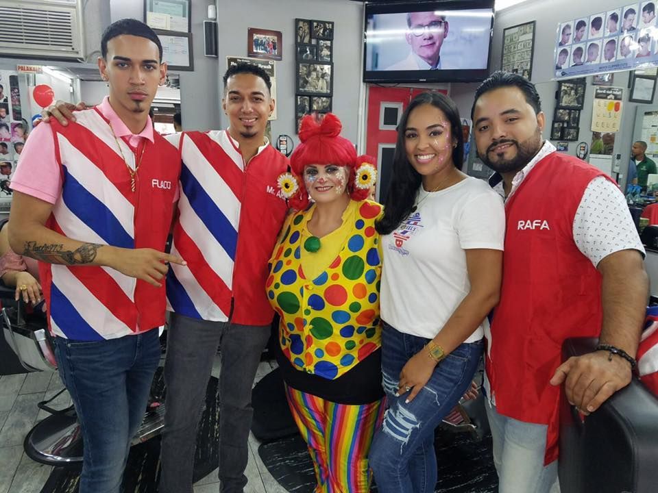 Five people posing in a barbershop, wearing colorful red, white, and striped clothing with one dressed as a clown.