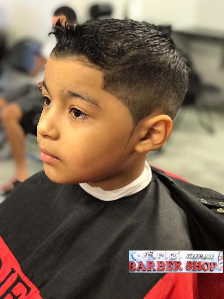 Child with a fresh fade haircut in a black barber cape, looking to the side in a barbershop.