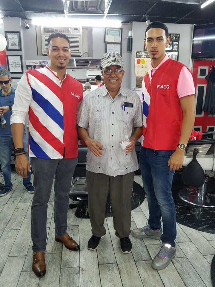 Three men standing together indoors, smiling in casual shirts in a small shop or office.