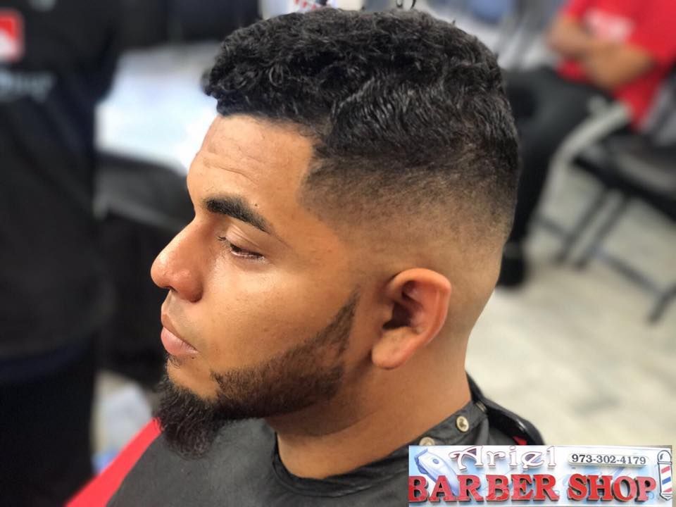 Man with a fresh fade haircut and beard in a barbershop, shown in side profile.