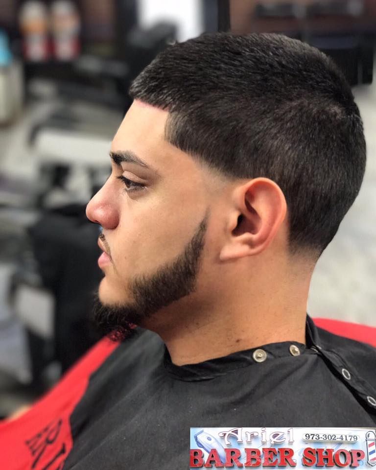 Profile view of a man with a fresh fade haircut and trimmed beard in a barbershop chair