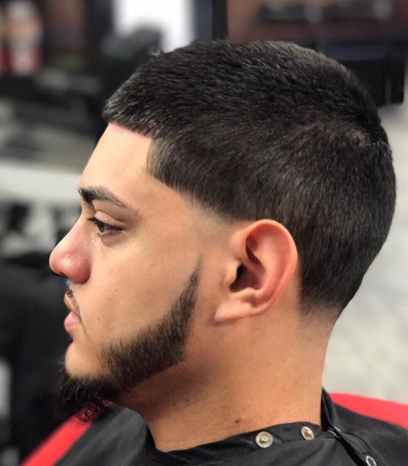 Profile view of a man with a short fade haircut and trimmed beard in a barber chair