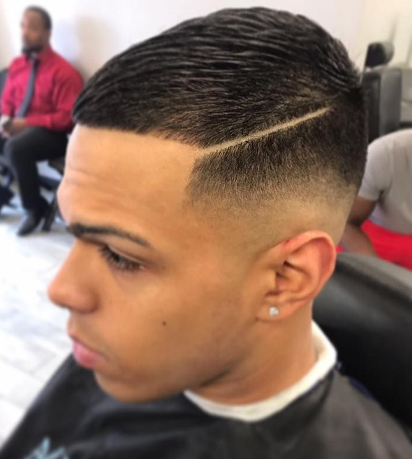 Close-up of a man with a sharp fade haircut and shaved side part in a barbershop chair